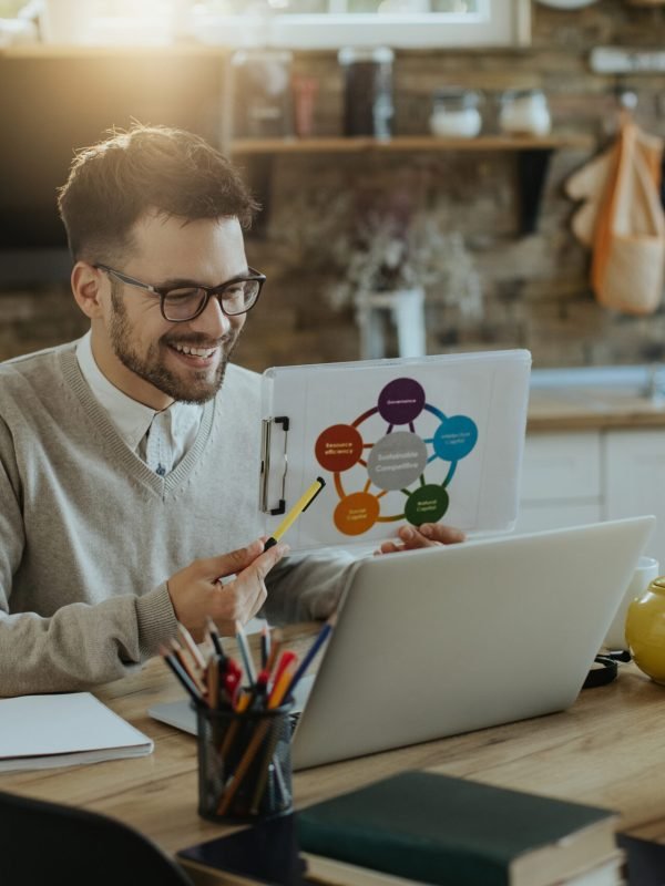 Happy businessman using computer and analyzing charts during conference call at home.